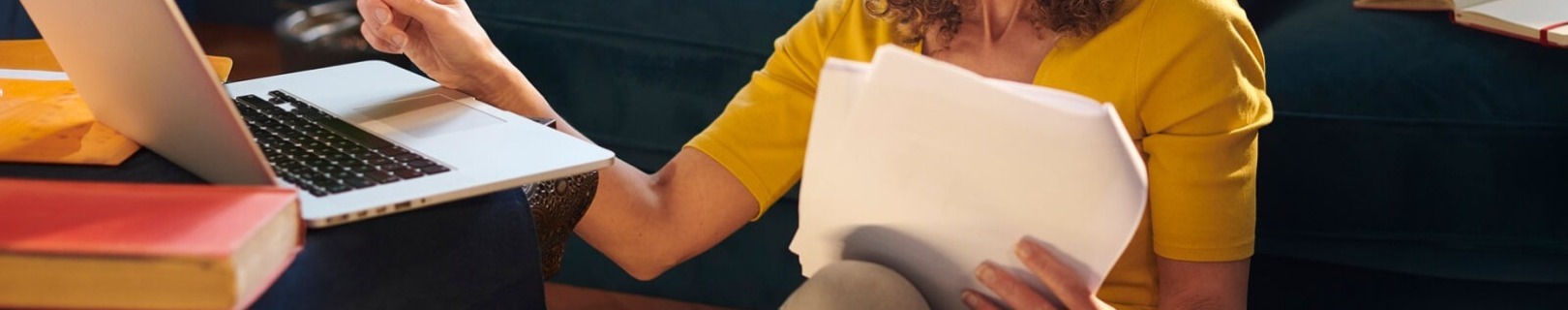 A young woman looking at papers and using a laptop