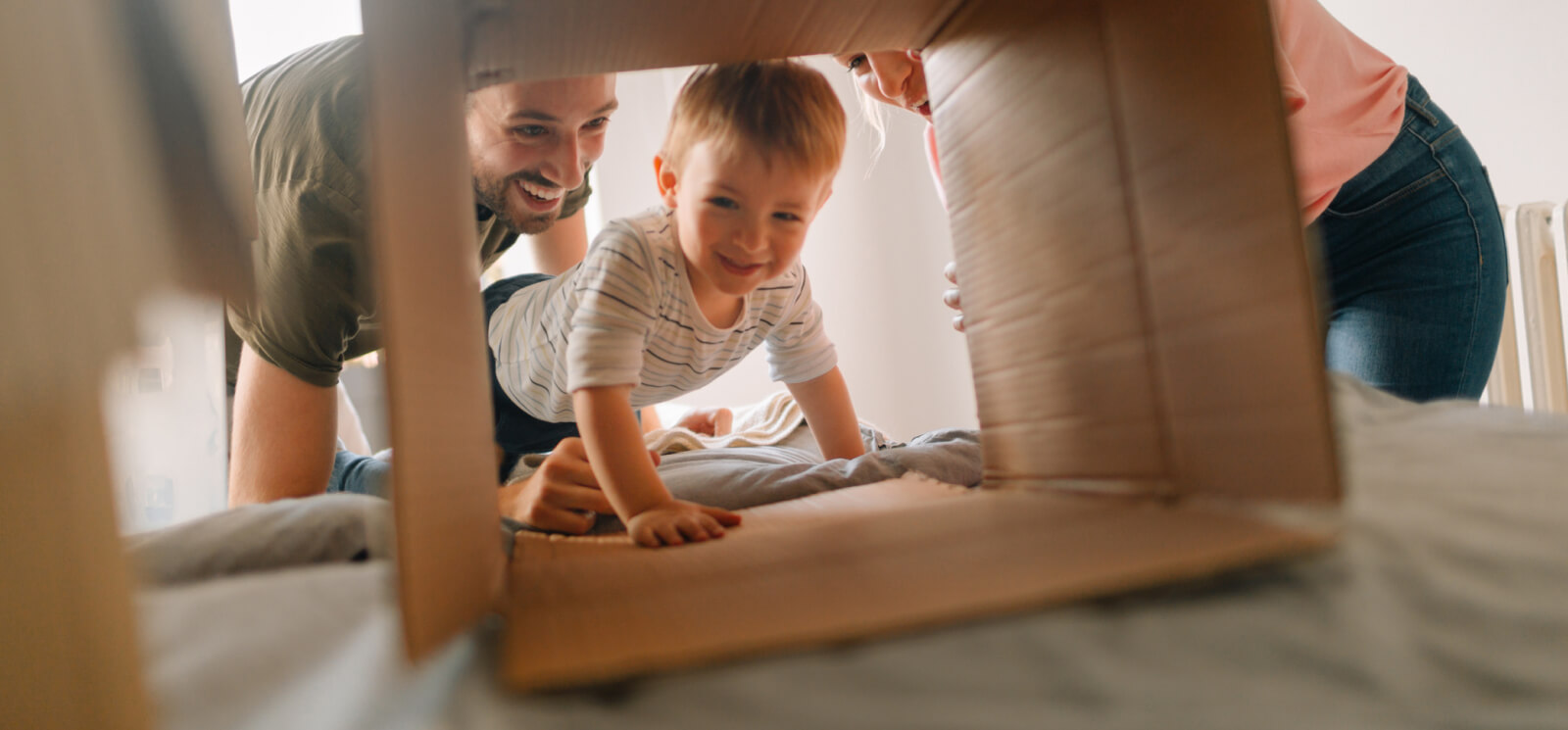 Young parents and a toddler playing with a cardboard box